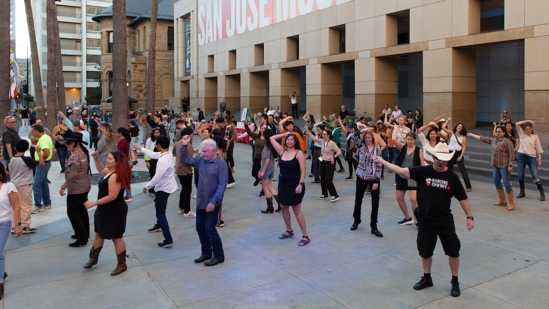 group of people dancing led by a White man wearing a western cowboy hat