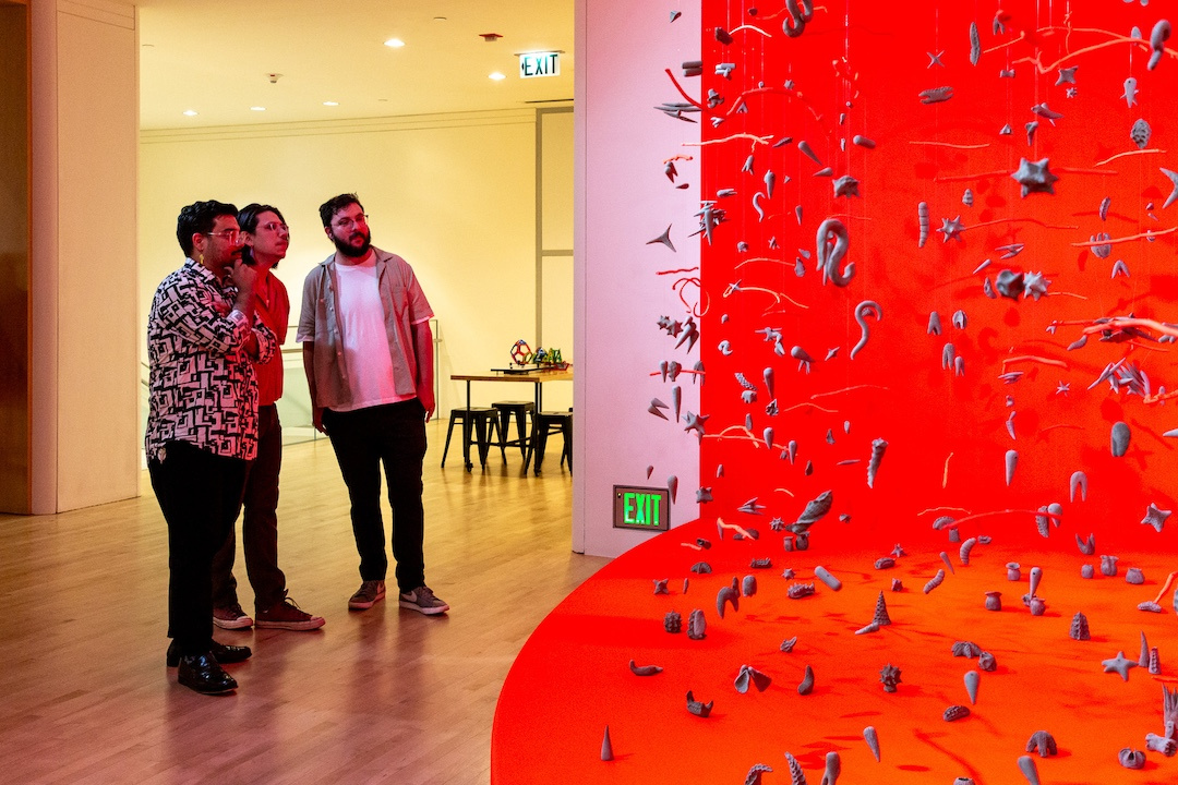 visitors gazing at a vibrant red installation of suspended clay objects