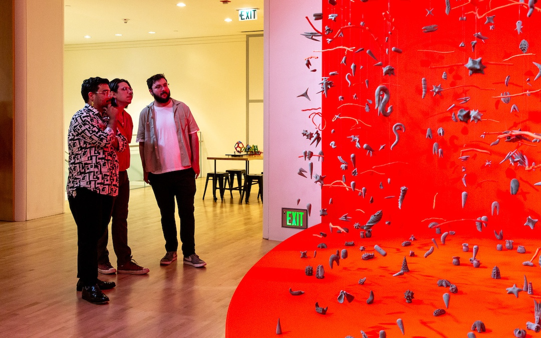 visitors gazing a vibrant red installation of suspended clay objects 