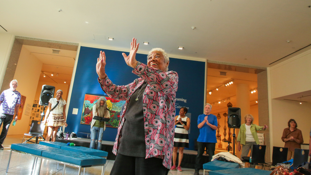 an older black woman dancing with a group of people singing behind her