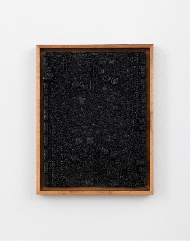 Against a white wall hangs a wooden frame. Inside is charcoal colors mixed within a black background.