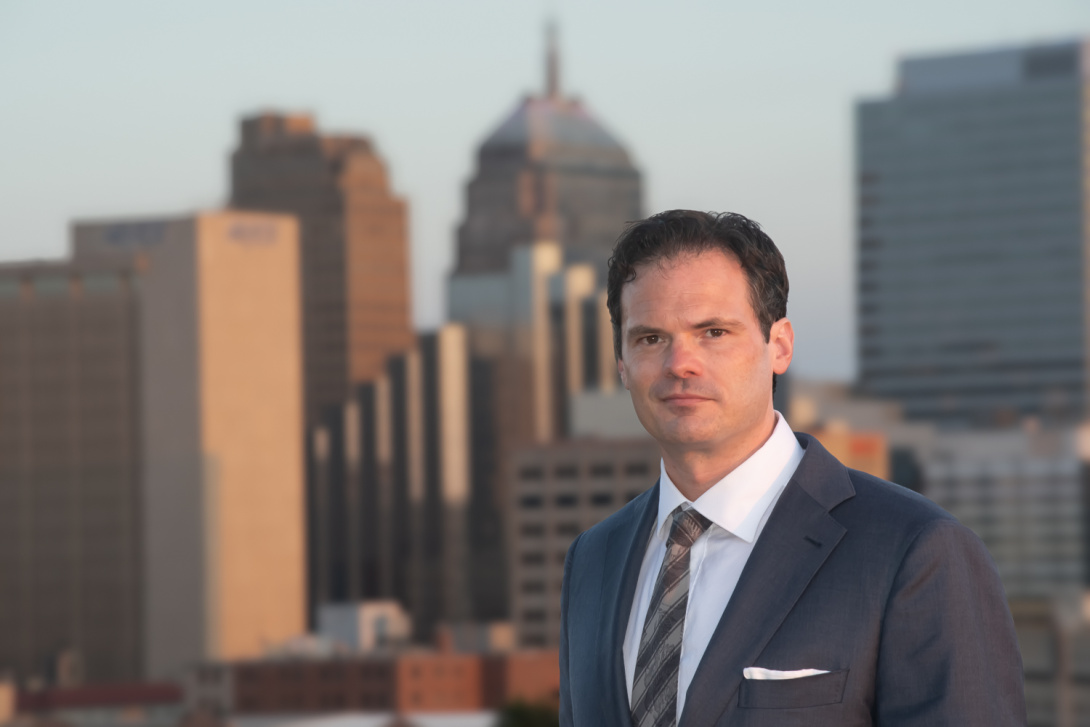 white man in a gray suit in front of a cityscape 