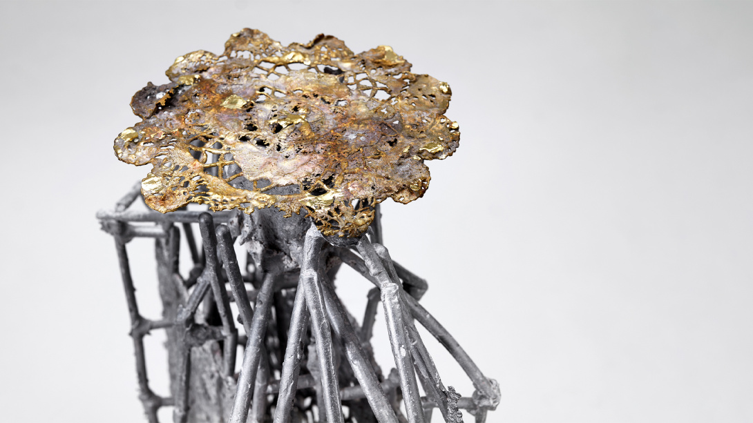 a crocheted wire flower casted in bronze on top of cast sticks