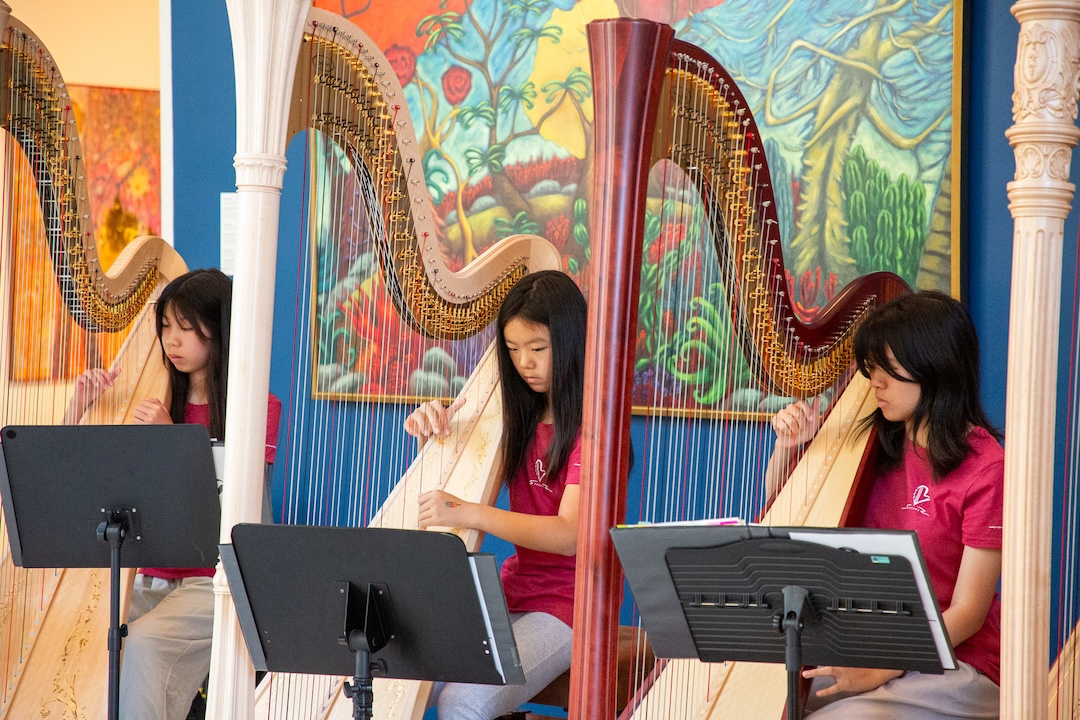 youth harpists playing harps in front of a lush painting