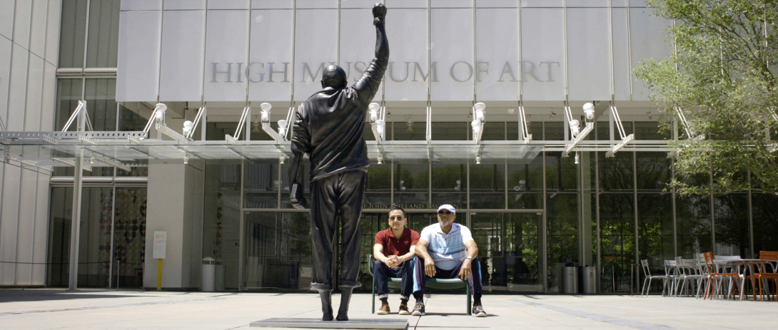 Two people seated at a bench gazing at a statue with a raised fist