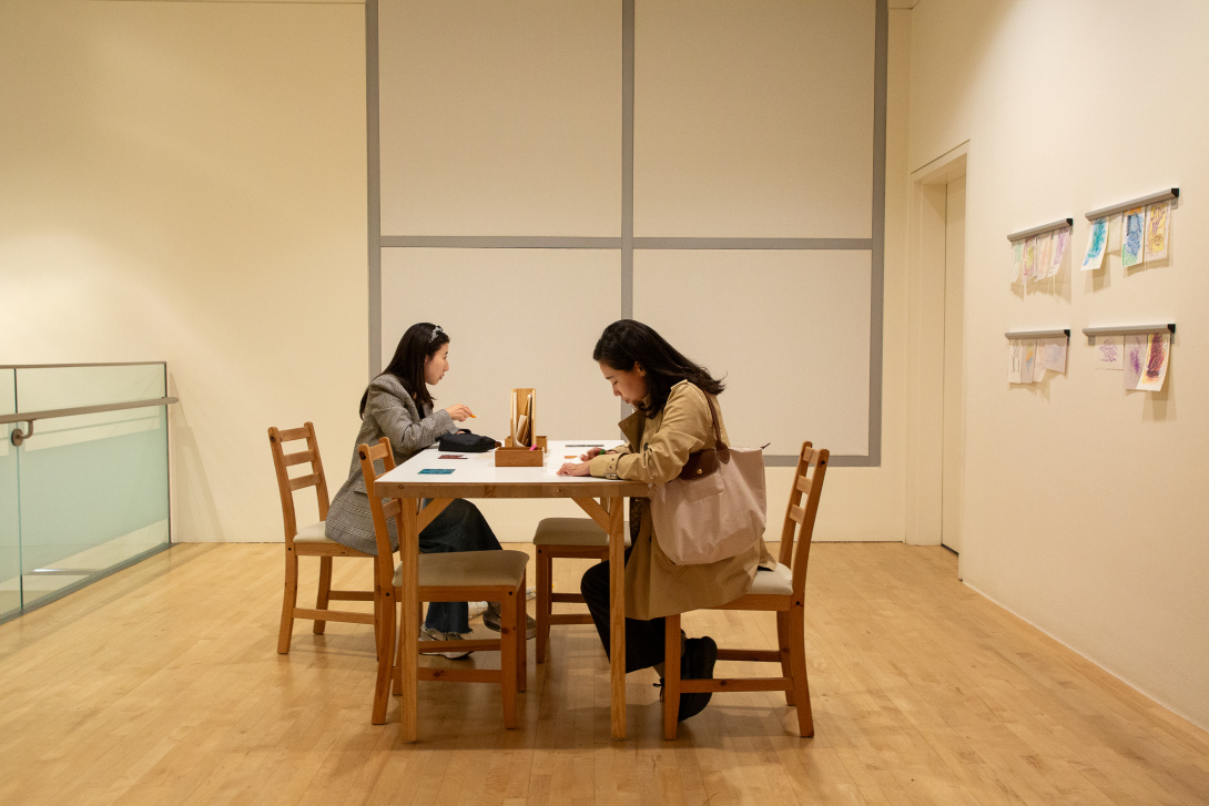 Two visitors seated at a table in a gallery activity space.