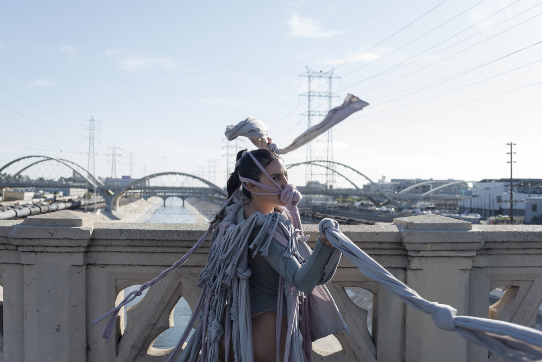 A woman walking on a bridge with pieces of cloth tied around her body and hair