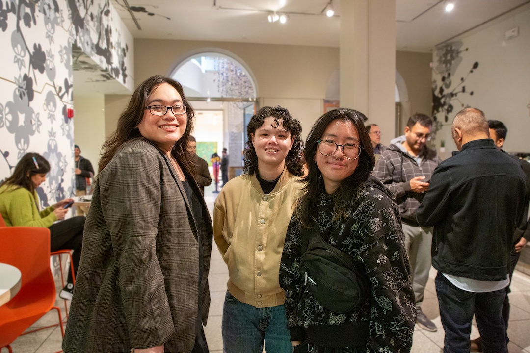 three queer and trans folks of asian descent smiling in a busy museum cafe