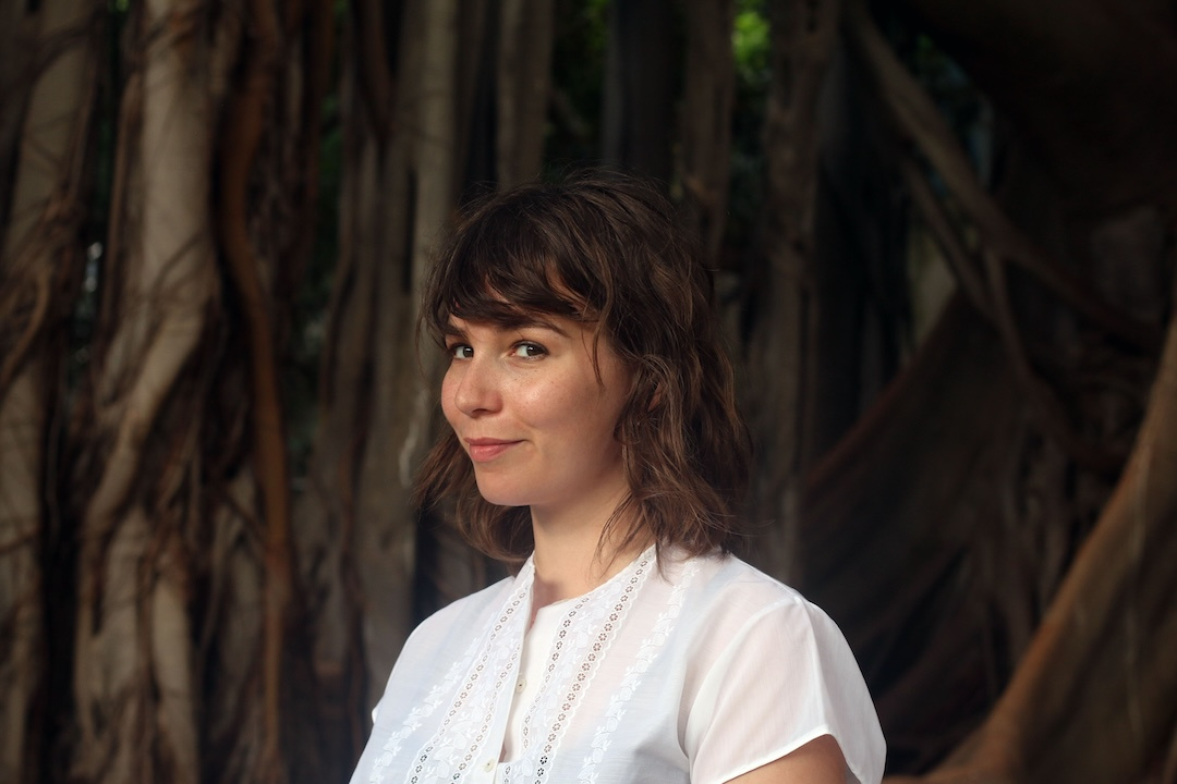 european women with brown short wavy hair wearing a white top with a gold necklace
