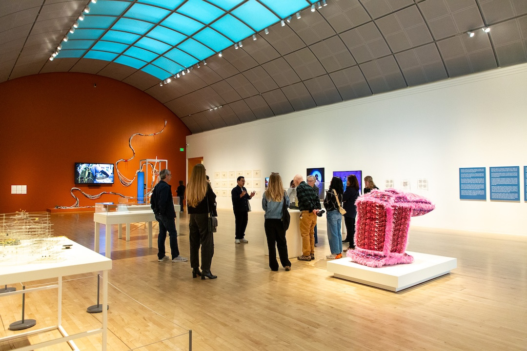 group of visitors in a large gallery listening intently to a person speaking