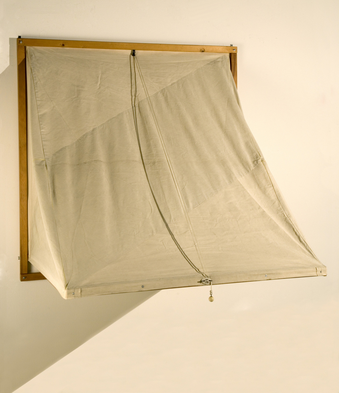 At first glance, it resembles a window being shaded from outside light. Upon closer inspection, it is a square, wooden frame with a piece of canvas being held by thin rope. 