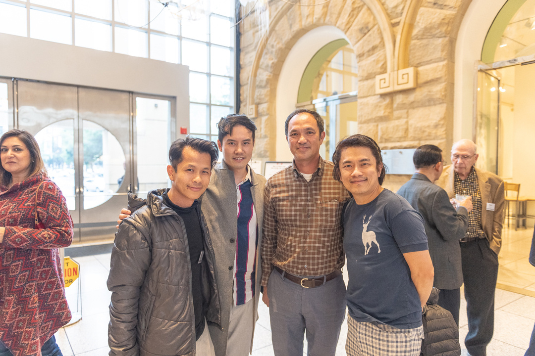 A group of 4 men, dressed casually in the lobby of the San José Museum of art, smile at the camera. Several other visitors mill around in the background of the photo.