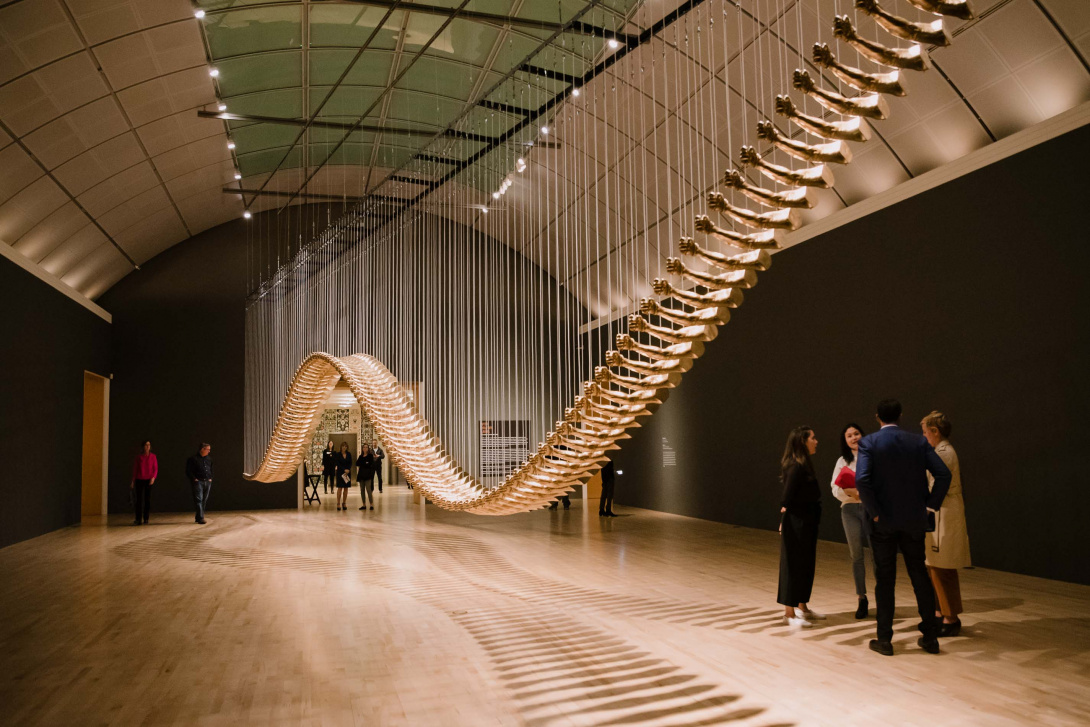 A large scale installation stretching across a grand gallery composed of golden arms. 