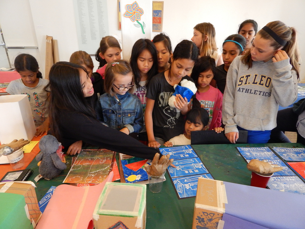 Children and teens convening on a table with art and crafts.