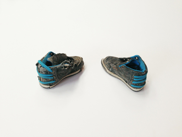 A child's high top sneakers arranged as if toes are pointing towards each other. Laces are removed from their usual position and used to tie the heel of the shoe. The laces and inside of the shoes are blue.