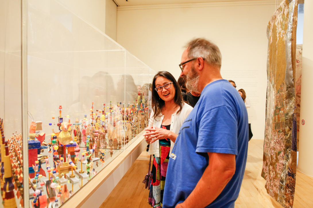 Woman with glasses in gallery with a gray-haired man in a blue t-shirt in a gallery.