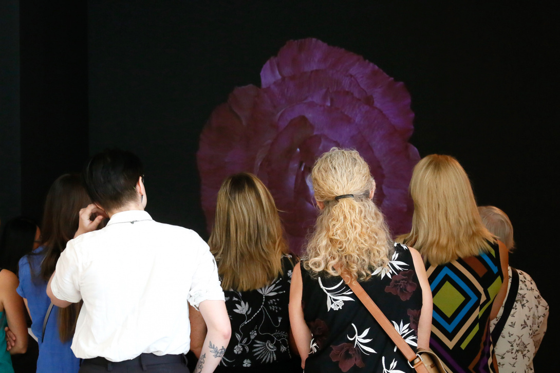 Visitors looking at a digital projection of a flower in a dark gallery.