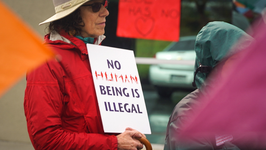 Woman holding up sign that states "No human being is illegal."