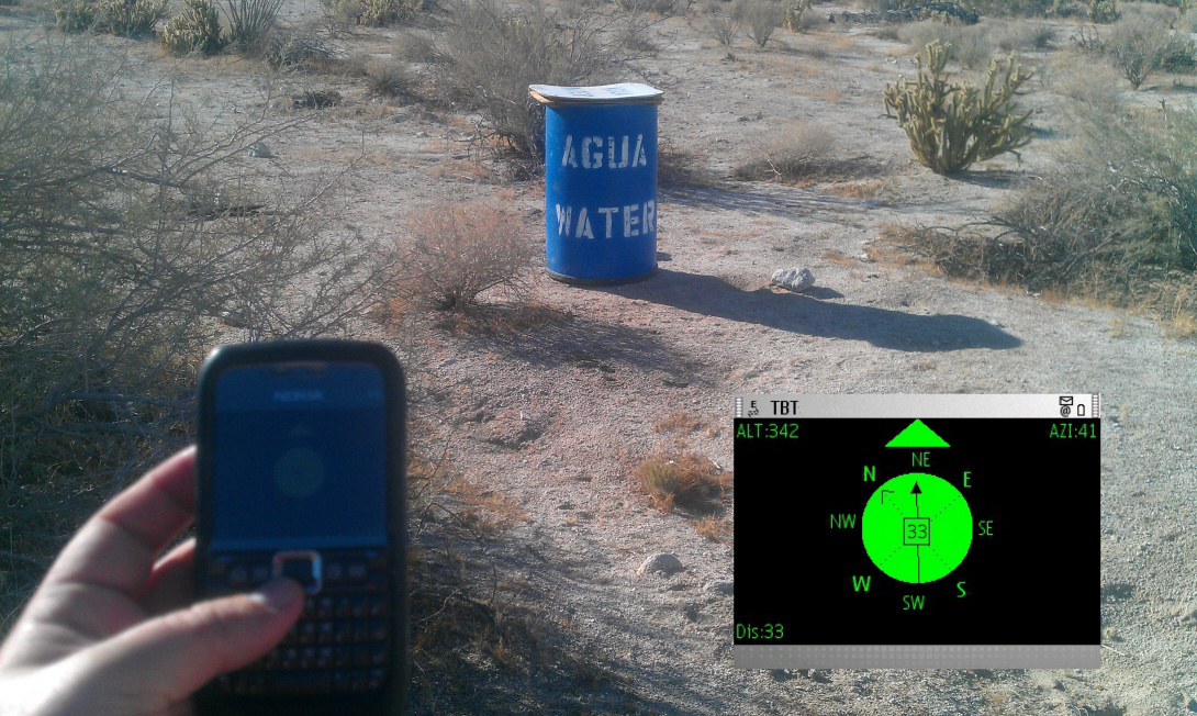 A photograph of a hand holding a Blackberry phone that displays a compass pointing towards a blue tin barrel. The image seems to have been taken in a desert. To the right, overlaid on the photograph, is a close-up of the Blackberry's compass display.