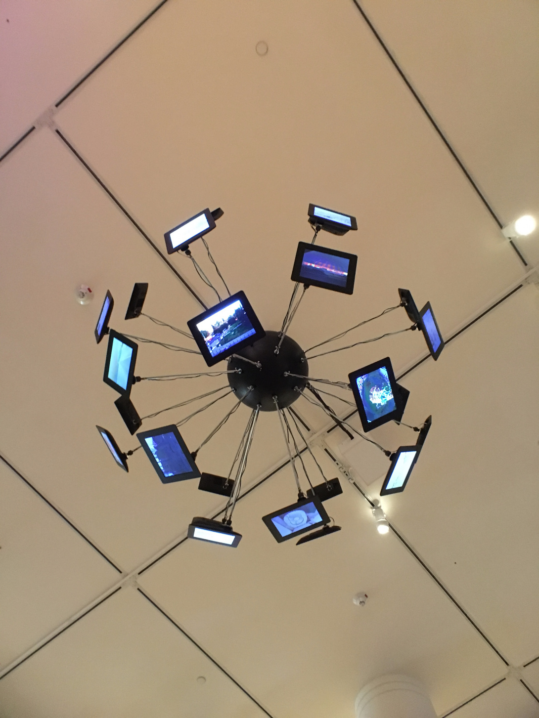 A photograph of a black ball hanging from the ceiling. It has multiple screens sticking out from it. The view is from below, looking up at all the screens.