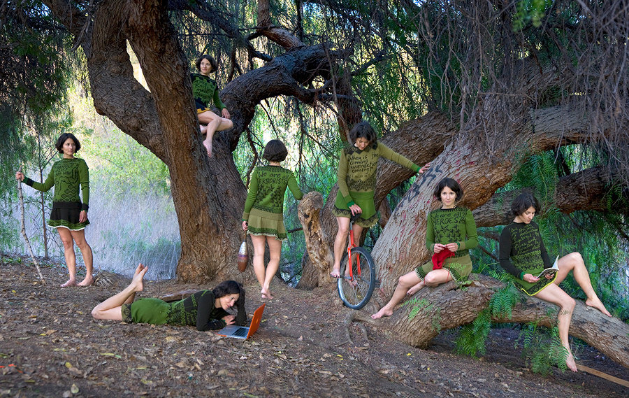 In nature, set against large trees, 7 nearly identical women read, look away, lay on the dirt with a laptop, sit on top of a high branch, sit on a low branch, and hold onto another nearby tree. All figures wear similar versions of the same long-sleeved skirted outfit.