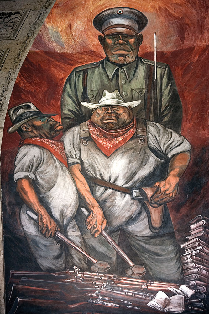 A mural of a soldier wearing army clothing. Two men stand in front of him wearing cowboy hats, guns in holsters, and bright bandanas around their necks. There are piles of guns in front of them and a stack of books to the right. 