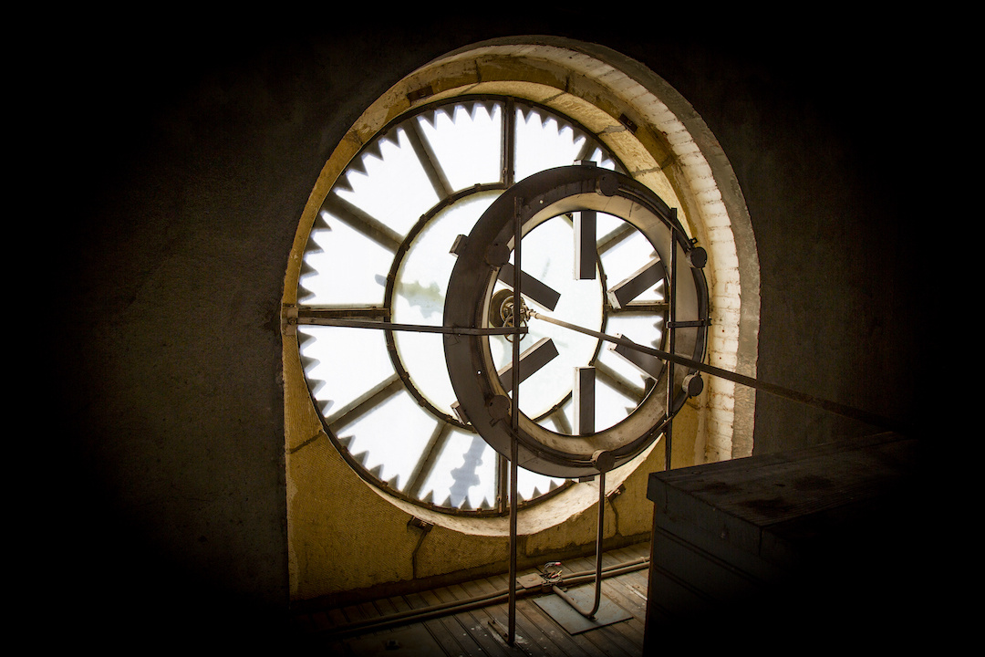 A clock face from behind with a ring shaped light in front and clock arms shadows.