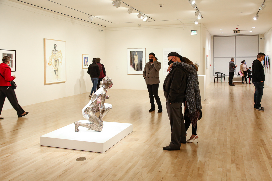  A couple intimately looking at a kneeling figurative sculpture by Manuel Neri, with an onlooker listening to an audio work.