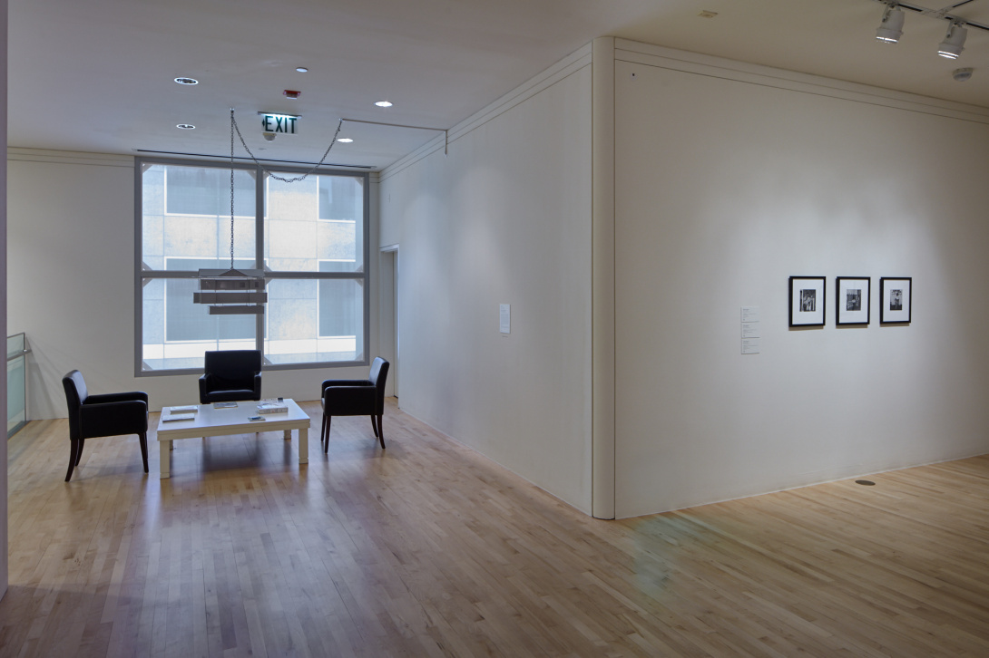 A seating area with three chairs and a coffee table with books. To the right of the room are three framed artworks that are hung on the wall.