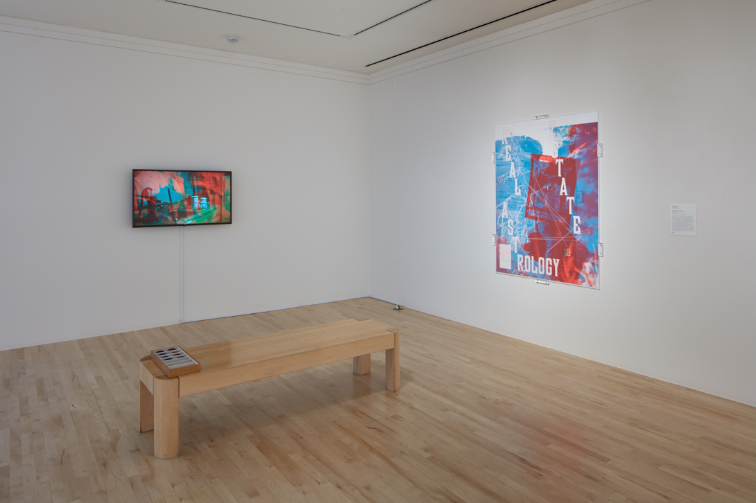 A photograph of a museum gallery. A 3D video screen is hung on the wall with a bench that is holding a box of 3D glasses. To the right there is a large paper work with the words "REAL ESTATE ASTROLOGY".