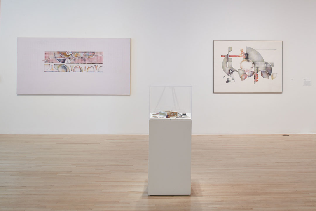 A pedestal housing small artifacts sits in a white walled gallery, framed between two large works on the wall. The hanging works have soft muted colors of pink and green with ample negative space. The designs are geometric and ethereal.