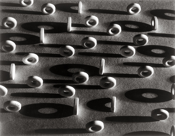 A black and white image of circular white lifesaver candies. They are sitting on their edges, casting shadows. The angle is taken from above, at a bit of a distance, making them look like tiny white car tires.