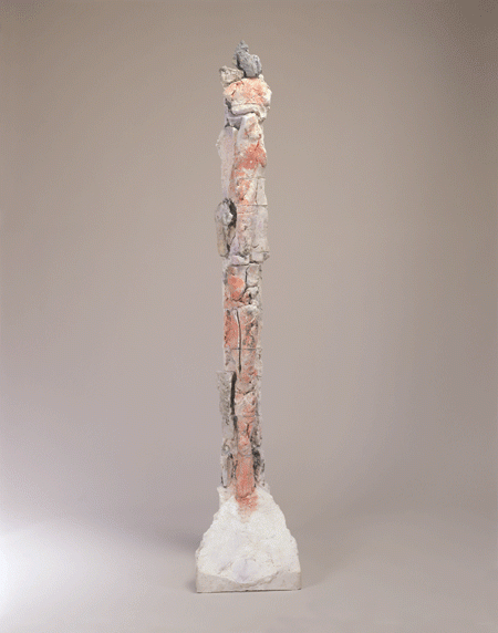 Pieces of human-like ceramic shards stacked together vertically like a tower. The structure is held by a white piece of ceramic or clay as the base.