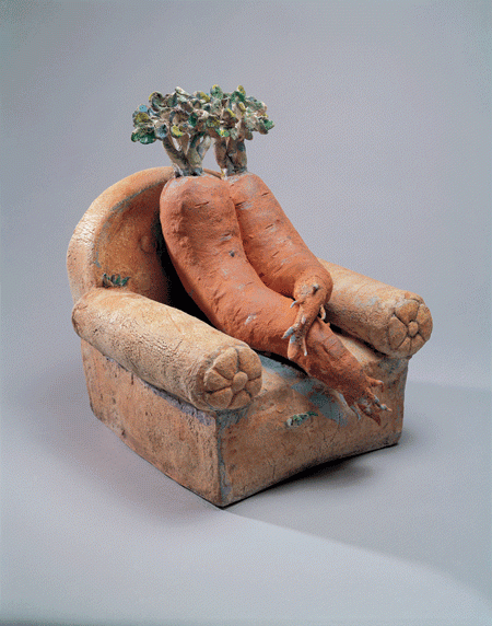 Two sleeping ceramic carrots cuddle on a single ceramic sofa chair. Both carrots have stocky green tops like two mini trees. They may have slept on it for so long that weeds started growing from them.