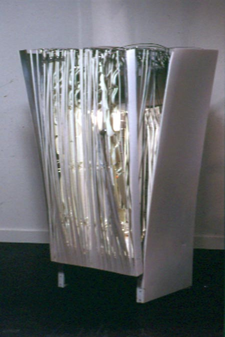 A deconstructed cabinet-looking fridge. Wires surround it and stick out on the top. There are two side metal corrugated panels holding the structure together but looks expanded on the top.