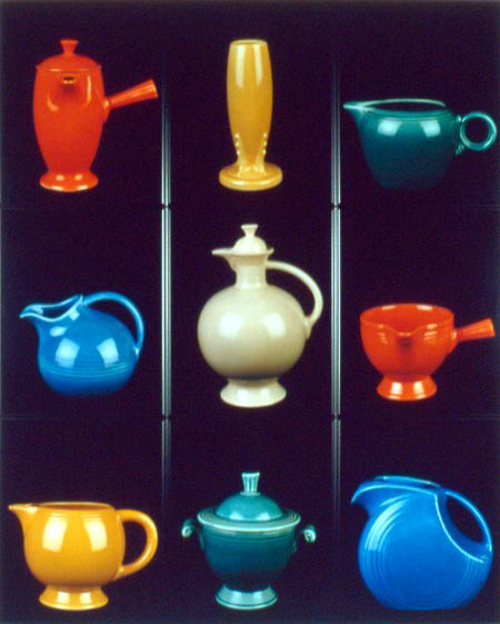 Nine bright colored pots and pitchers of varying shapes and sizes on three different levels, with two metallic looking poles dividing them. The pots and pitchers are glazed in different colors and reflect the light shining on it.