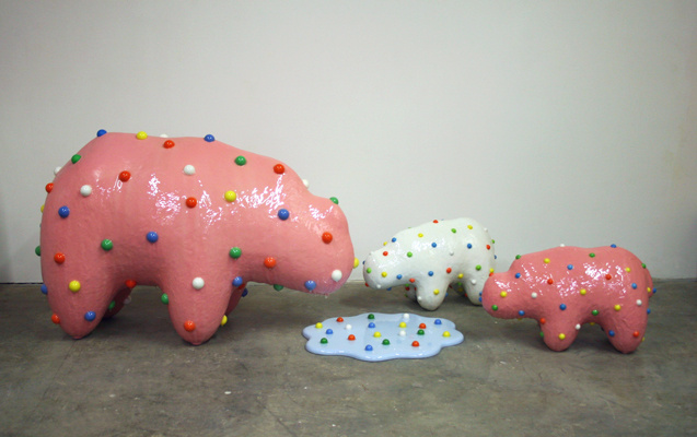A photograph of three animal cookies surround a bluish puddle with rainbow spots like the candy speckles on the animals. They animal cookies are white and pink.