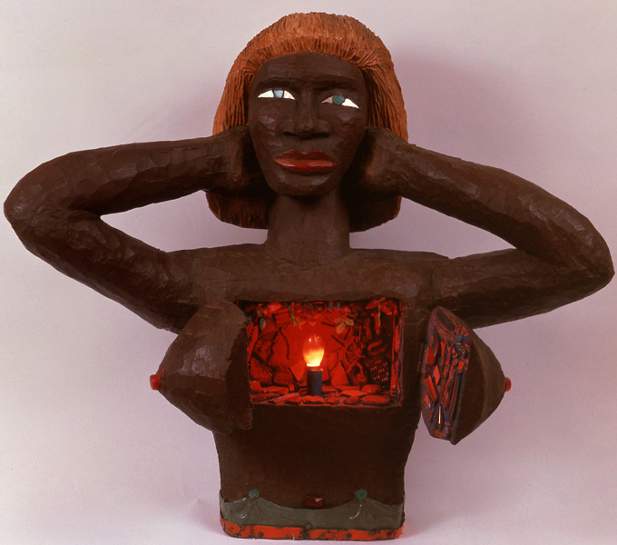 A clay model of a Black woman with her chest cut open to reveal a light as if inside a cave. The woman has her hands covering her ears. It looks like she is trying to keep the noise out to keep the flame in her heart alive. 