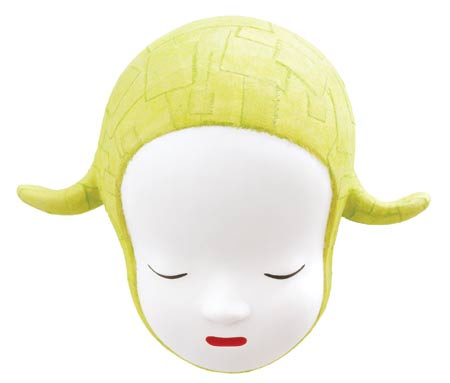 A ceramic face bows their round porcelain white head. Their eyes are closed and calm in thought—maybe sad, in concentration, or resting. Their lips are a small red line. They wear a bright yellow bonnet with small playful fabric lamblike ears. 