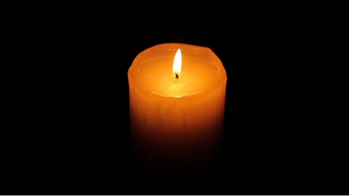 A photograph of red cylindrical candle with a single burning flame that sits at the center of a black background.