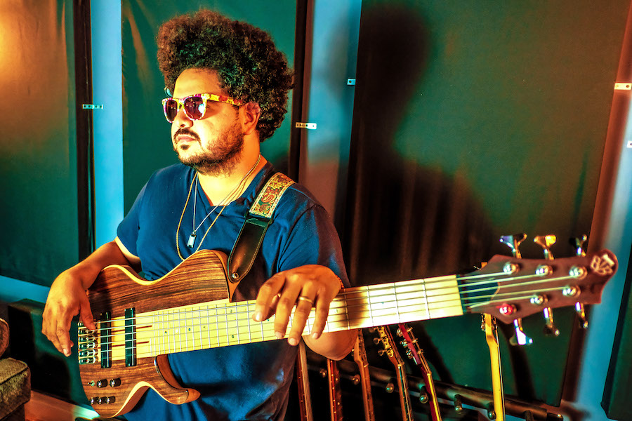 Man with afro and sunglasses holding up an electric bass.