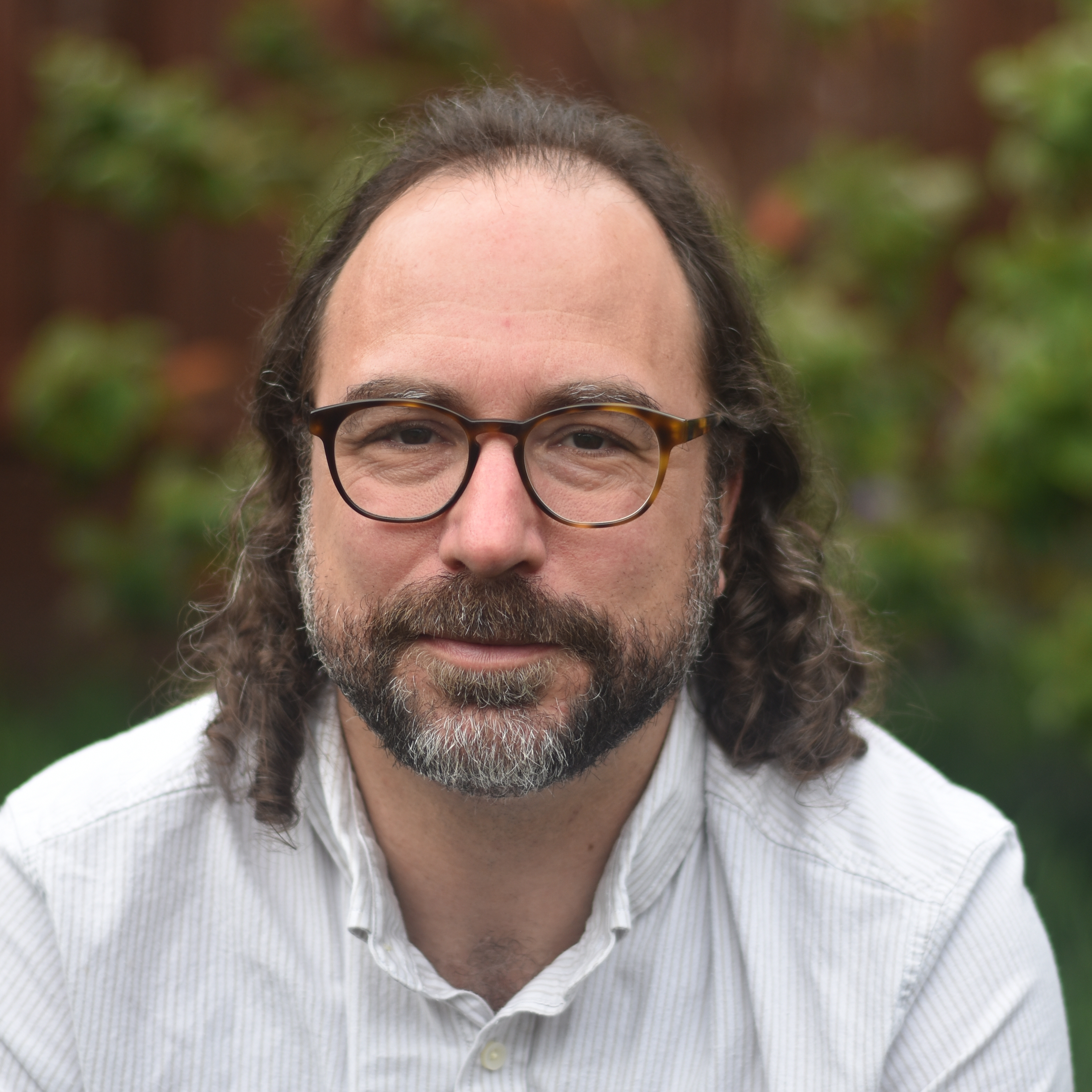 a bearded man wearing glasses with long curly hair